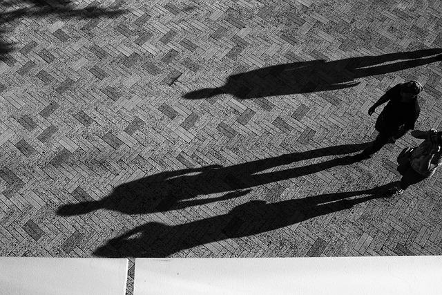 Long shadows of 3 people on an inlaid brick floor.