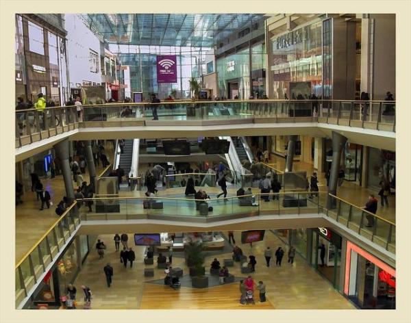 Inside a 3-level shopping mall with escalators and people walking.