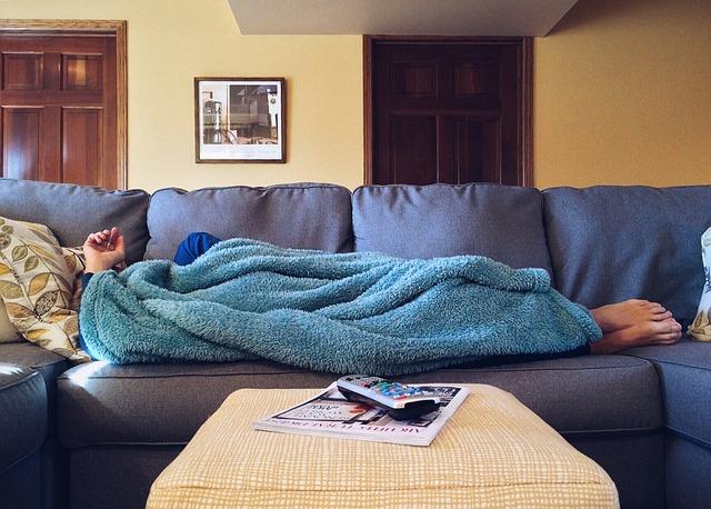 A blue sofa with a sleeping man under a blue blanket, bare feet poking out.