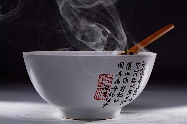 A steaming soup bowl viewed from the side, so you can't see what the soup looks like.