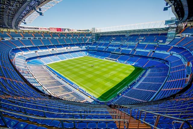 A picture of blue stadium seats around an empty green soccer pitch.