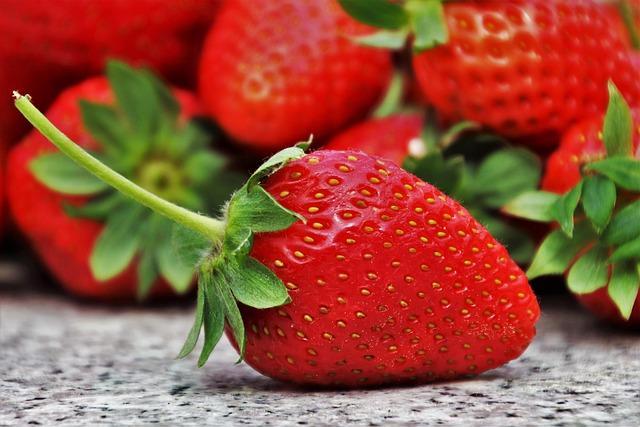 A close-up of strawberries on a counter - stems still on, uncut, piled high.