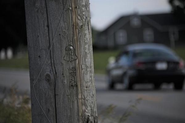 Wooden telephone pole is in focus, a car driving away is blurry.