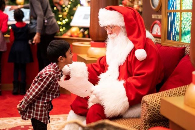 A mall Santa talking to a young boy standing in front of him.