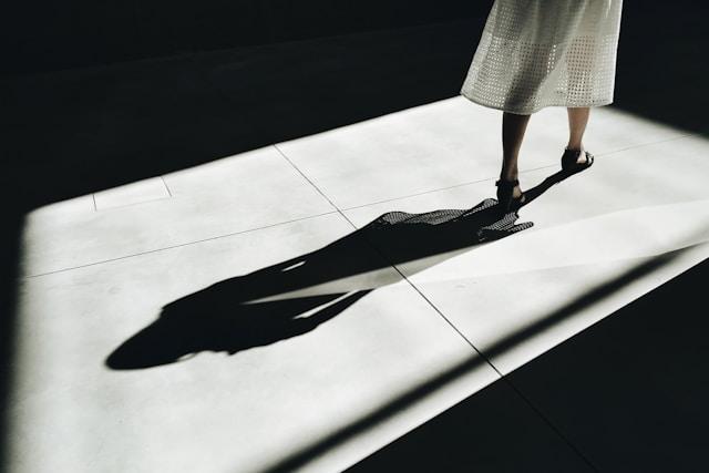 A woman walking out of the shot, but her entire shadow is visible behind her on the lit floor.