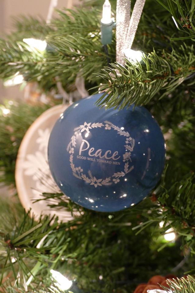 A blue Christmas ball hanging on a tree with the word "peace" clearly visible.