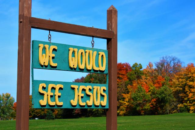 A sign on green boards with yellow letters that reads, "We would see Jesus."