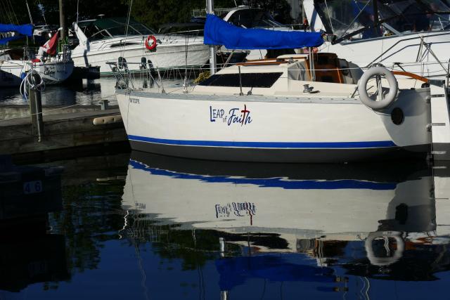 A white sailboat moored in a slip, reflection visible, sail neatly packed away, name visible on the side - "Leap of Faith"