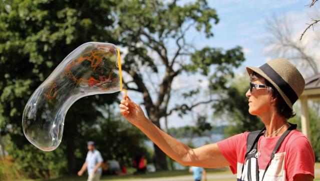 Susan herself with a large bubble wand and a giant bubble while at an outdoors event.