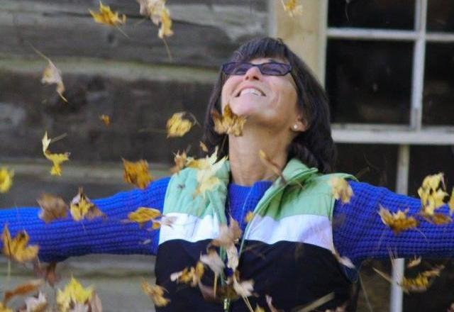 Susan herself looking up, arms outstretched, big smile, while a whole armful of leaves floats down on her.