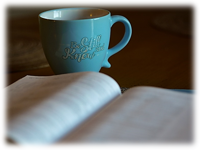 A cup of tea in a teal colored cup sitting on a table behind a Bible that is blurred.