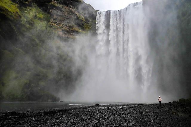 Looking up to a massive waterfall from a rocky beach at the bottom.