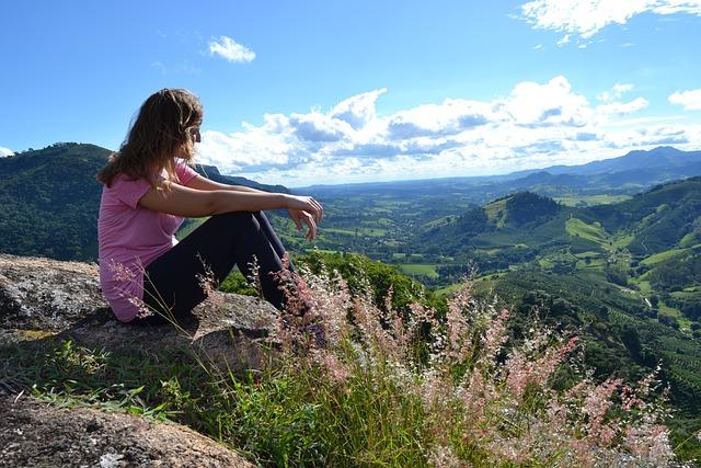 A woman sitting on a mountain top looking out over a valley.