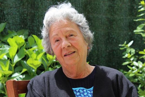 Woman with short, grey hair  and a sweatshirt, no glasses and a kindly half-smile.