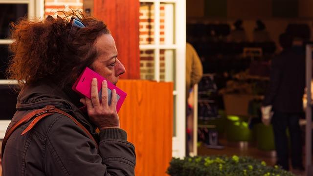 A middle-aged woman walking along a street with a pink phone to her ear.