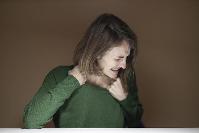 A woman with a green sweater, pulling at the neckline, looking away in pain.