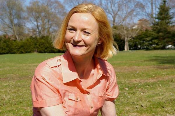 Middle-aged woman with shoulder length blond hair and a smile on a sunny day in a grassy park.