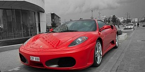 A red ferrari F430 parked out front of a car dealership.