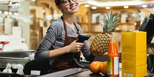 Young woman at a grocery check-out lane preparing to scan a pineapple.