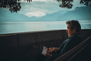 An AI image of an old man sitting looking out across a lake.