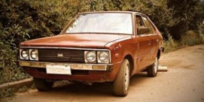 Old, run-down reddish-brown 1975 Hyundai Pony parked at the side of the road.