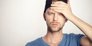 A man in a blue shirt and baseball cap turned backwards doing a palm slap to his forehead in confusion.