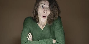 A middle-aged woman with her arms crossed looking directly at us, surprised.