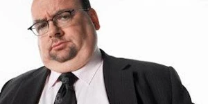 A stout man with glasses, suit and tie, looking down at us with confidence.