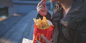 A close up of a woman holding a large container of McDonald french fries with one hand and eating one with the other.