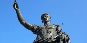 A bronze statue of Caesar against a clear blue sky.