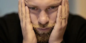 A man resting his face in his hands so that his face is stretched taut and there are wrinkles by his temples.