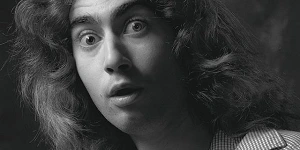 A black and white image of a young man with long wavy hair looking very alarmed.