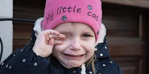 A young girl in a pink woolen hat and a winter coat, crying.