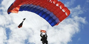 A red and blue parachute against a scattered cloudy blue sky.