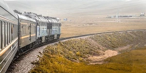 A train rounding a gentle curve on flat land from the perspective of one of the train cars about 3 cars back from the engine.