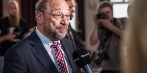 A photo of politician Martin Schulz listening to a question before answering into a mic inside a building.