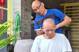 A bald man with glasses running a razor over the head of another elderly bald man.