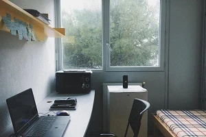 A wall-desk, single chair, open laptop and a small bed in a small room.