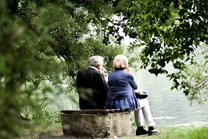 An elderly couple sitting on a concrete bench beside some water.