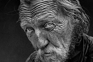 A black and white photo of an old man with very wrinkly skin, a scruffy beard and unkempt hair.