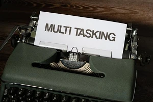 An old-fashioned green typewriter with "multi tasking" written in a large font and all caps on a piece of paper in the machine.