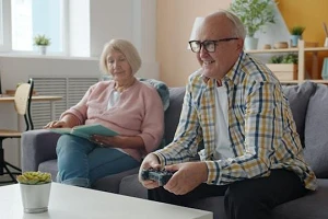 An elderly couple sitting on their couch, smiling at something in front of them.