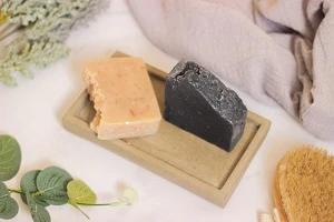 A photo of 2 types of homemade soap - light brown and black - on a wooden tray.