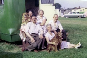 A photo from the 1950s showing an extended family of 5 with their 2 dogs outside their camper trailer.