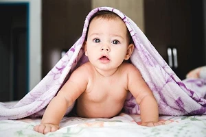 A young baby on its tummy under a purple blanket draped over its head and body.