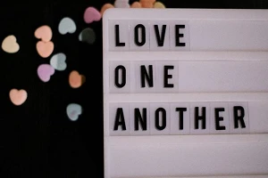 A letter-slide sign that reads "Love One Another" on a black background with several small colored hearts.