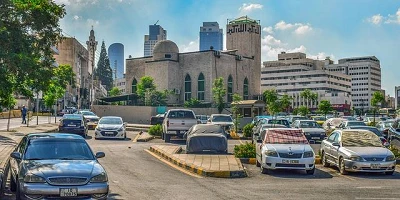 A parking lot in a large city with several cars parked in the stalls.
