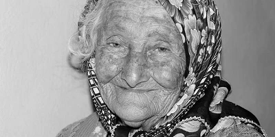 A black and white image of an old woman wearing a head scarf.