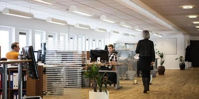 A large open office with someone walking through looking over at people in their work stations.