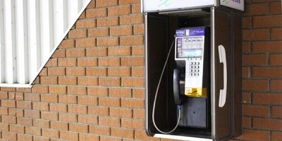 A telus payphone outside on a brick wall.